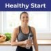 A woman in athletic wear holding a water bottle in a bright kitchen with fresh fruit.