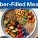 An overhead bowl holds lentils, chickpeas, vegetables, berries, seeds, and grains beneath a blue headline.