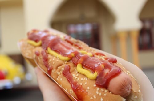 A hot dog on a white plate beside a red soda cup.